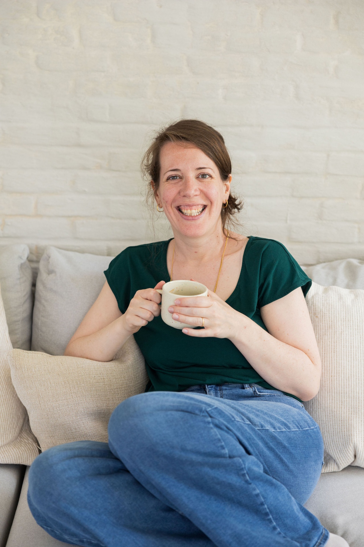 Ann lachend op de zetel met een koffietas