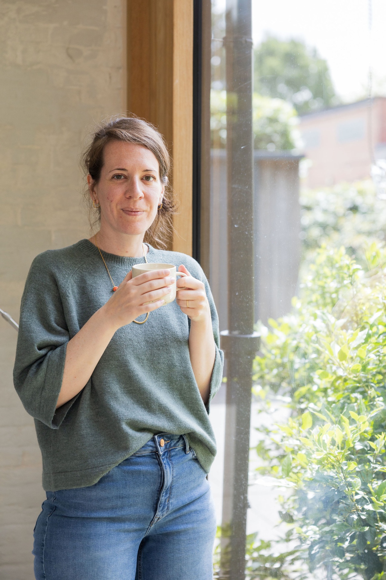 Ann bij het raam met een koffie in de handen